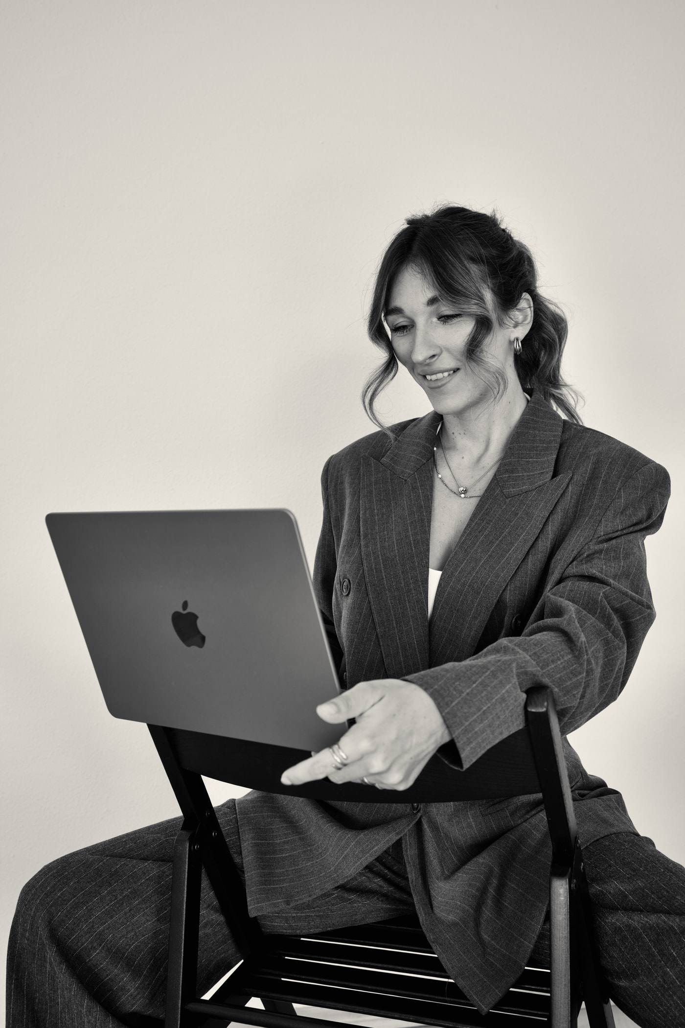 Steffi Cebis sitzt rittlings auf einem Stuhl, den Laptop auf der Rückenlehne, und zeigt lächelnd auf den Bildschirm.